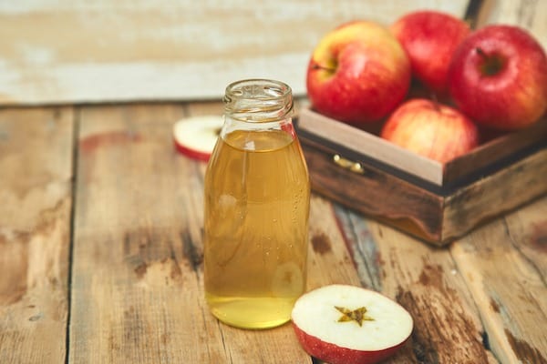 apple cider vinegar and red apples on wooden bench