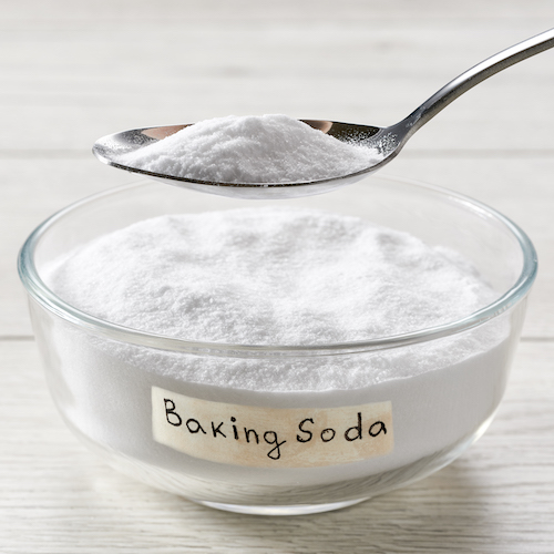 Close-up of baking soda on spoon against background of bowl on wooden table.